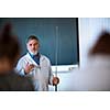 Senior chemistry professor giving a lecture in front of classroom full of students (shallow DOF; color toned image)