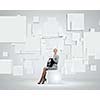 Image of elegant businesswoman sitting on white cube touching media button