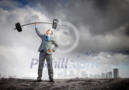 Image of strong businessman lifting barbell above head with one hand Image of strong businessman lifting barbell above head with one hand