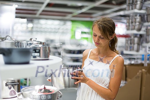 Pretty, young woman choosing a the right pot for her cooking in a modern home furnishings store (color toned image; shallow DOF) Pretty, young woman choosing a the right pot for her cooking in a modern home furnishings store (color toned image; shallow DOF)