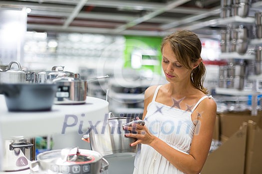 Pretty, young woman choosing a the right pot for her cooking in a modern home furnishings store (color toned image; shallow DOF)