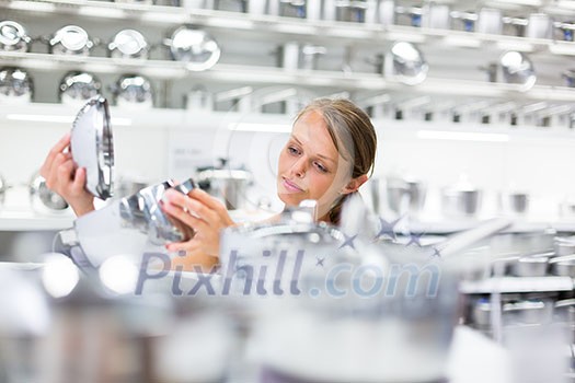 Pretty, young woman choosing a the right pot for her cooking in a modern home furnishings store (color toned image; shallow DOF) Pretty, young woman choosing a the right pot for her cooking in a modern home furnishings store (color toned image; shallow DOF)