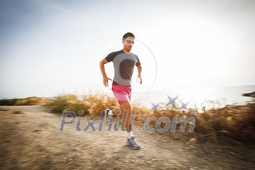 Caucasian young man running on a seacost path on a lovely summer evening, training for marathon (motion blurred image)