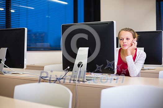 Pretty, young female college student using a desktop computer/pc in a college library (shallow DOF; color toned image)