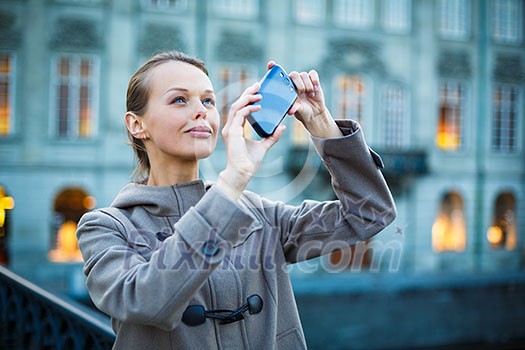 Elegant, young woman taking a photo with her cell phone camera while travelling (shallow DOF; color toned image)