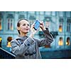 Elegant, young woman taking a photo with her cell phone camera while travelling (shallow DOF; color toned image)