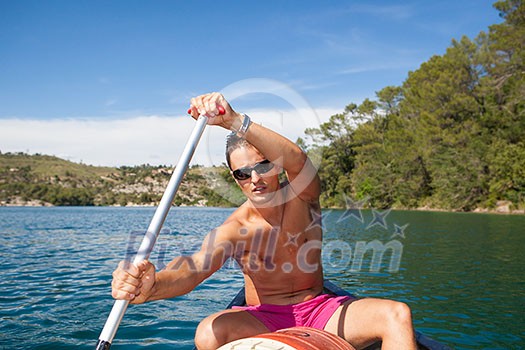 Handsome young man on a canoe on a lake, paddling, enjoying a lovely summer day