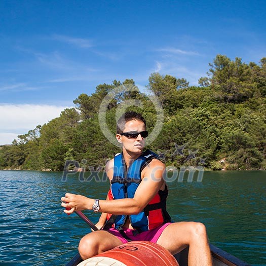 Handsome young man on a canoe on a lake, paddling, enjoying a lovely summer day Handsome young man on a canoe on a lake, paddling, enjoying a lovely summer day