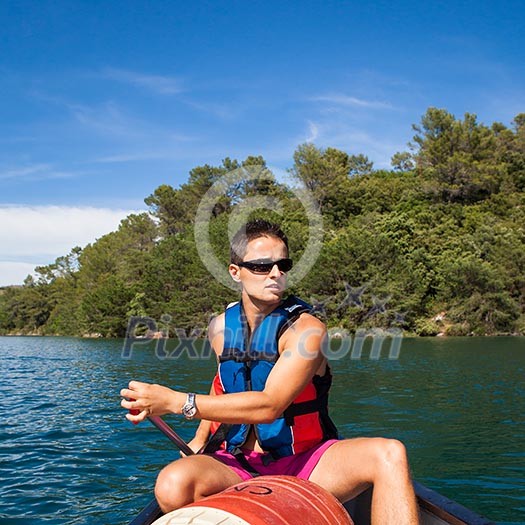 Handsome young man on a canoe on a lake, paddling, enjoying a lovely summer day