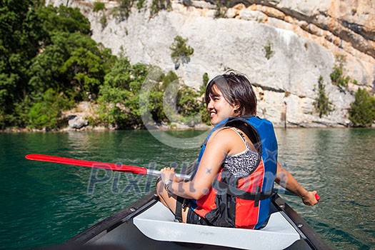 Pretty, young woman on a canoe on a lake, paddling, enjoying a lovely summer day
