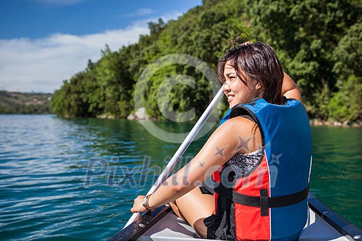 Pretty, young woman on a canoe on a lake, paddling, enjoying a lovely summer day Pretty, young woman on a canoe on a lake, paddling, enjoying a lovely summer day