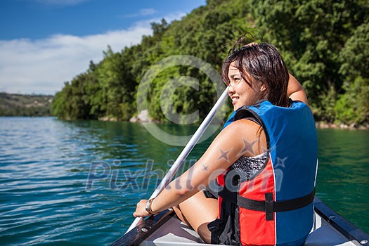 Pretty, young woman on a canoe on a lake, paddling, enjoying a lovely summer day