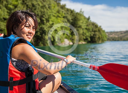 Pretty, young woman on a canoe on a lake, paddling, enjoying a lovely summer day Pretty, young woman on a canoe on a lake, paddling, enjoying a lovely summer day