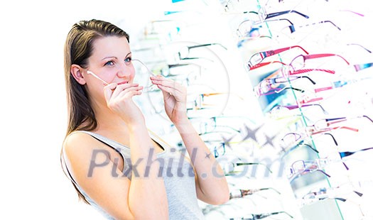 Pretty, young woman choosing new glasses frames in an optician store (color toned image; shallow DOF)