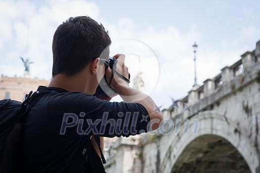 Portrait of a handsome young tourist taking photographs while sightseeing in Rome, Italy (with the Sant'Angelo bridge and castel in the background)