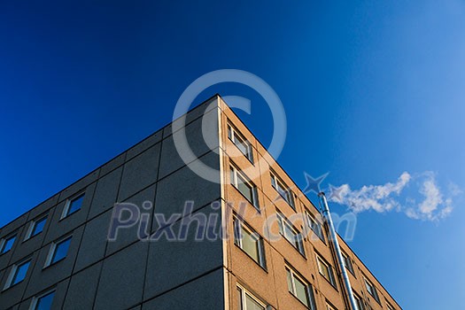 Heating in freezing winter temperatures: smoke/flue gases going out of a chimney by an apartment building against blue sky