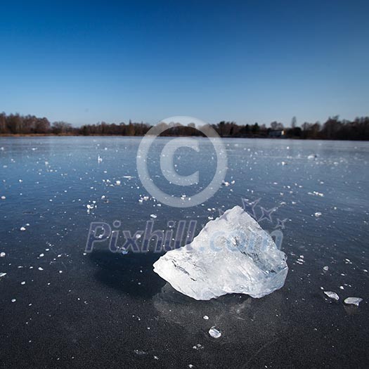 Freezing winter temperatures: block of ice lying on the surface of a frozen pond on a sunny winter day