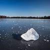 Freezing winter temperatures: block of ice lying on the surface of a frozen pond on a sunny winter day