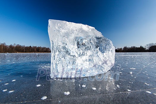 Freezing winter temperatures: block of ice lying on the surface of a frozen pond on a sunny winter day Freezing winter temperatures: block of ice lying on the surface of a frozen pond on a sunny winter day