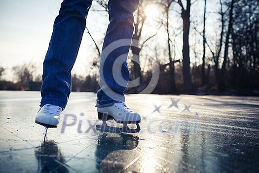 Young woman ice skating outdoors on a pond on a beautiful sunny day (selective focus)