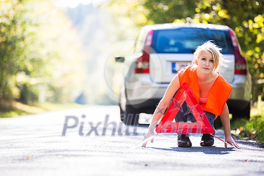 Young female driver wearing a high visibility vest, setting up the reflective trianglec after her car has broken down