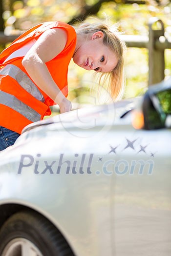 Young female driver wearing a high visibility vest on the roadside after her car has broken down