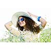 Young beautiful girl in hat and glasses sitting in grass