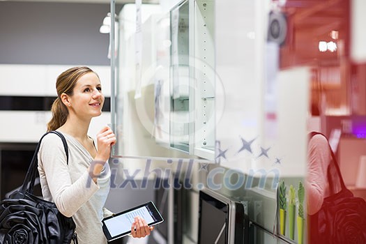 Young woman shopping for furniture in a furniture store, using her tablet computer to compare prices/check for dimensions