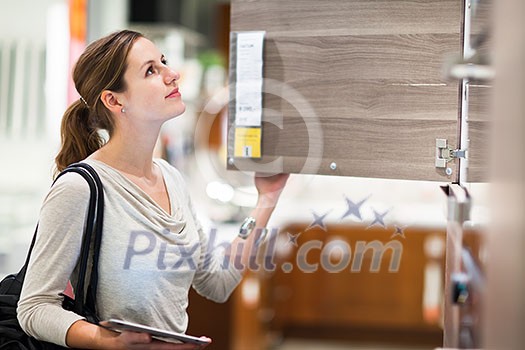 Young woman shopping for furniture in a furniture store, using her tablet computer to compare prices/check for dimensions