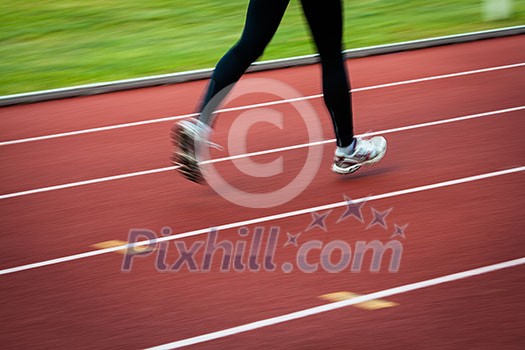 Young woman running at a track and field stadium (motion blurred image)