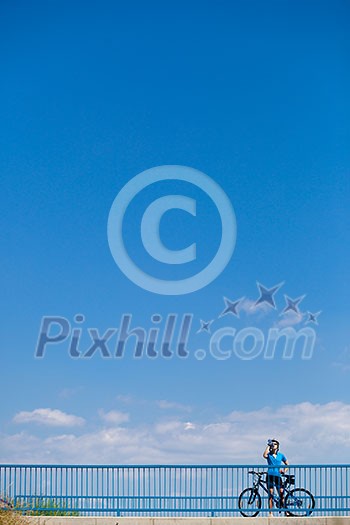 Background for poster or advertisment pertaining to cycling/sport/outdoor activities - female cyclist during a halt on a bridge against blue sky (color toned image) Background for poster or advertisment pertaining to cycling/sport/outdoor activities - female cyclist during a halt on a bridge against blue sky (color toned image)