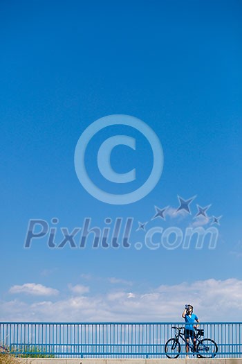 Background for poster or advertisment pertaining to cycling/sport/outdoor activities - female cyclist during a halt on a bridge against blue sky (color toned image)