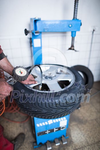 Auto mechanic in a garage checking the air pressure in a tyre with a pressure gauge  (shallow DOF; color toned image)