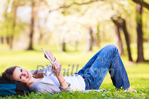 Young woman using her tablet computer while relaxing outdoors in a park on a lovely spring day Young woman using her tablet computer while relaxing outdoors in a park on a lovely spring day