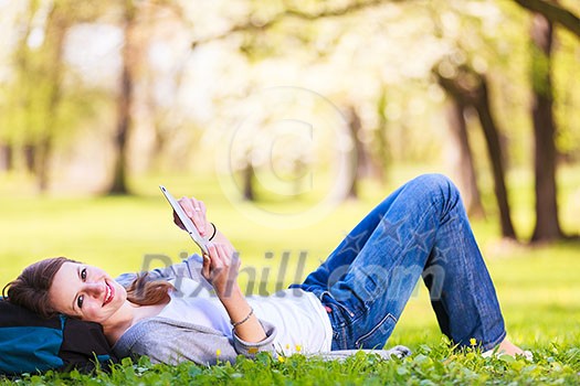 Young woman using her tablet computer while relaxing outdoors in a park on a lovely spring day