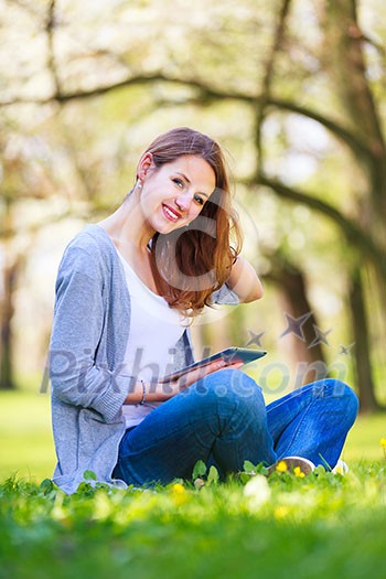 Young woman using her tablet computer while relaxing outdoors in a park on a lovely spring day