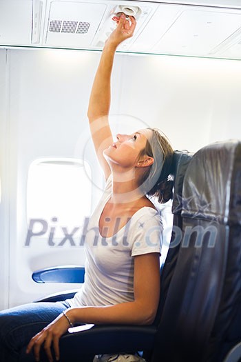 Female passenger adjusting air conditioning above her seat while on board of an aircraft