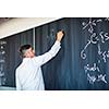 Senior chemistry professor writing on the board while having a chalk and blackboard lecture (shallow DOF; color toned image)