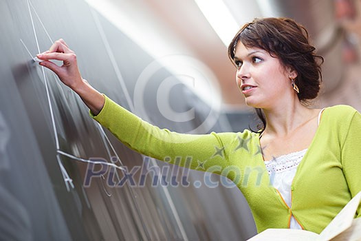Pretty young elementary school/college teacher writing on the chalkboard/blackboard during a math class (color toned image; shallow DOF)
