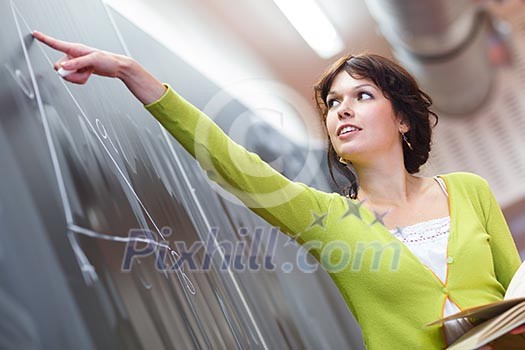 Pretty young elementary school/college teacher writing on the chalkboard/blackboard during a math class (color toned image; shallow DOF)