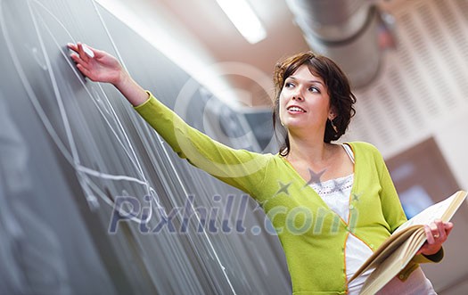 Pretty young elementary school/college teacher writing on the chalkboard/blackboard during a math class (color toned image; shallow DOF)