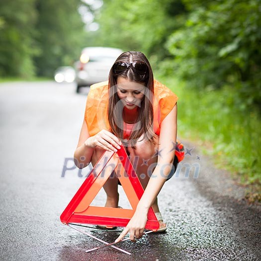 Young female driver wearing a high visibility vest, calling the roadside service/assistance after her car has broken down