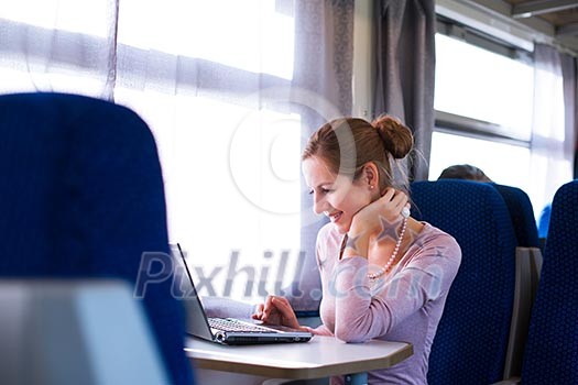Young woman using her laptop computer while on the train (shallow DOF; color toned image)