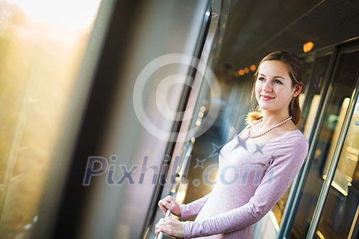 Young woman traveling by train, watching the passing country side while standing in the train corridor