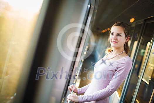 Young woman traveling by train, watching the passing country side while standing in the train corridor Young woman traveling by train, watching the passing country side while standing in the train corridor