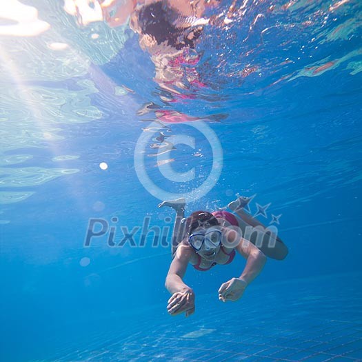 Underwater swimming: young woman swimming underwater in a pool, wearing a diving mask Underwater swimming: young woman swimming underwater in a pool, wearing a diving mask