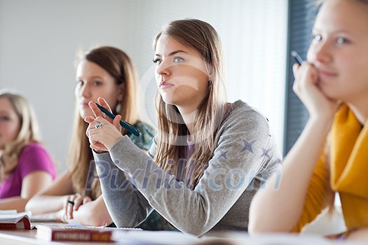 young pretty female college student sitting in a classroom full of students during class