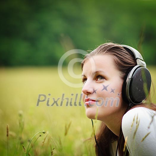 portrait of a pretty young woman listening to music on her mp3 player outdoors (daydreaming)