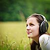 portrait of a pretty young woman listening to music on her mp3 player outdoors (daydreaming)