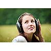 portrait of a pretty young woman listening to music on her mp3 player outdoors (daydreaming)